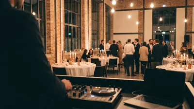 Soirée de séminaire dans une halle en briques, vue depuis la cabine du DJ, invités debout entre les tables
