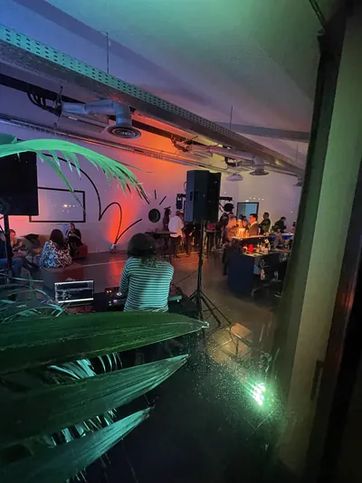 DJ de dos dans un loft, lumière orangée, invités autour du bar